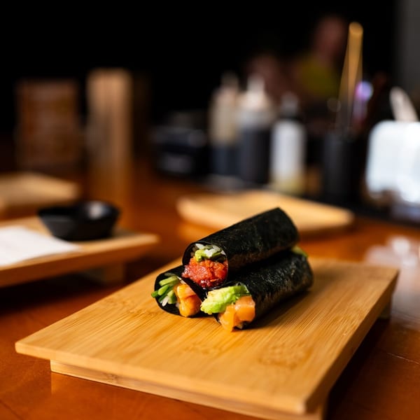 Two seaweed sushi hand rolls filled with salmon, avocado, cucumber, and vegetables on a bamboo board in a dimly lit restaurant.
