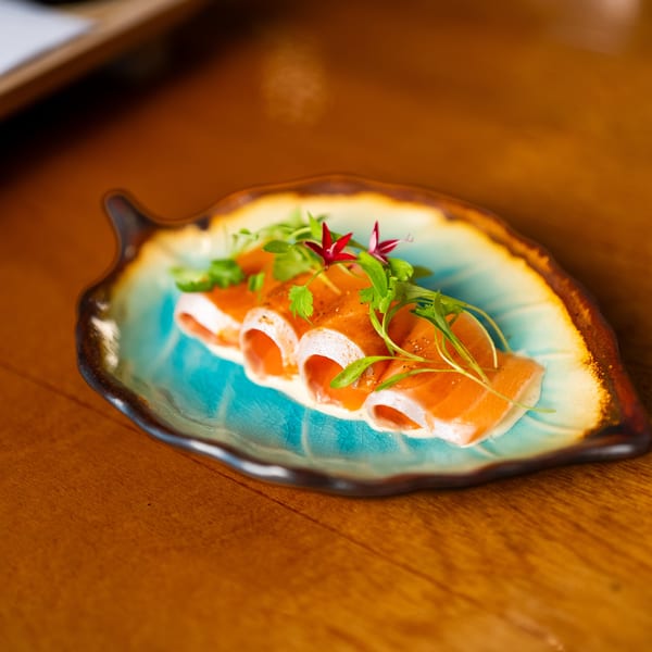 Smoked salmon rolls garnished with fresh herbs and edible flowers on a colorful ceramic plate atop a wooden restaurant table.
