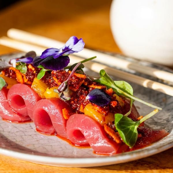 Colorful plated dish with pink pickled vegetables, roasted peppers, microgreens, and edible purple flowers on a ceramic plate.