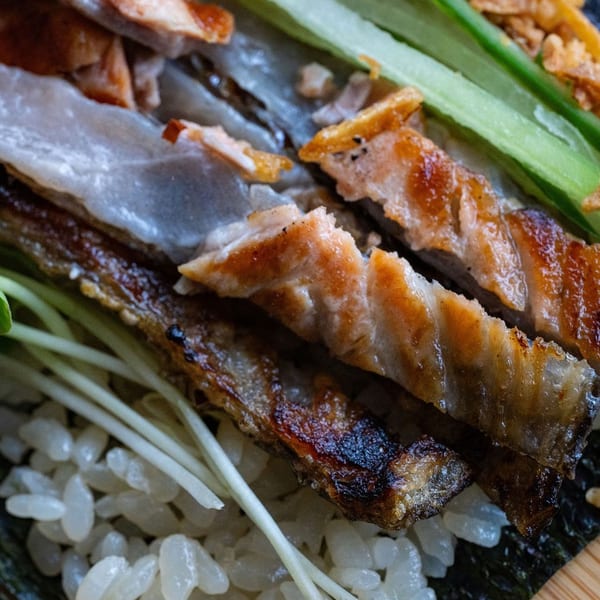 Close-up of grilled, glazed eel over sushi rice and nori, garnished with green onions.