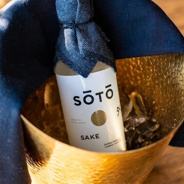 SOTO sake bottle nestled in a hammered gold ice bucket, draped with a navy cloth on a wooden table.
