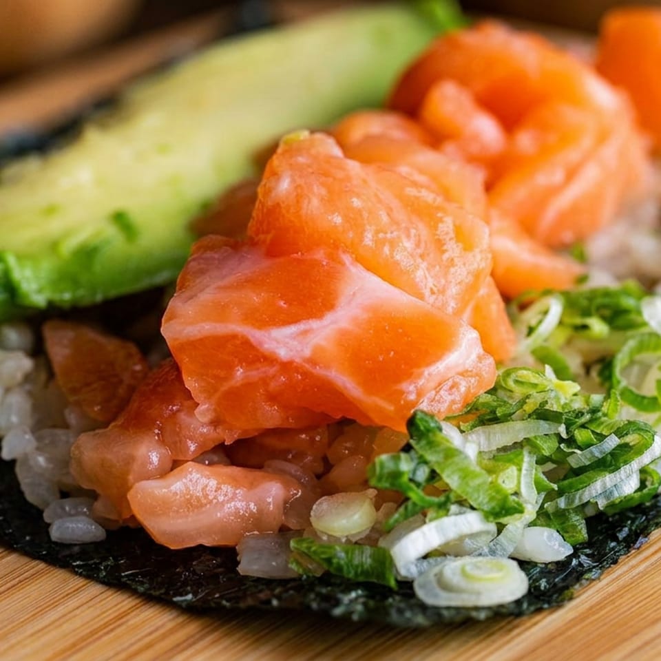 Close-up of a sushi hand roll with salmon, avocado, rice, seaweed, and sliced green onions on a wooden board.